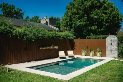 Pileta premium a medida con muro WPC, ducha de piedra y cantero decorativo integrada al jardín en Country Marcos Paz, Tucumán — Viejobueno
