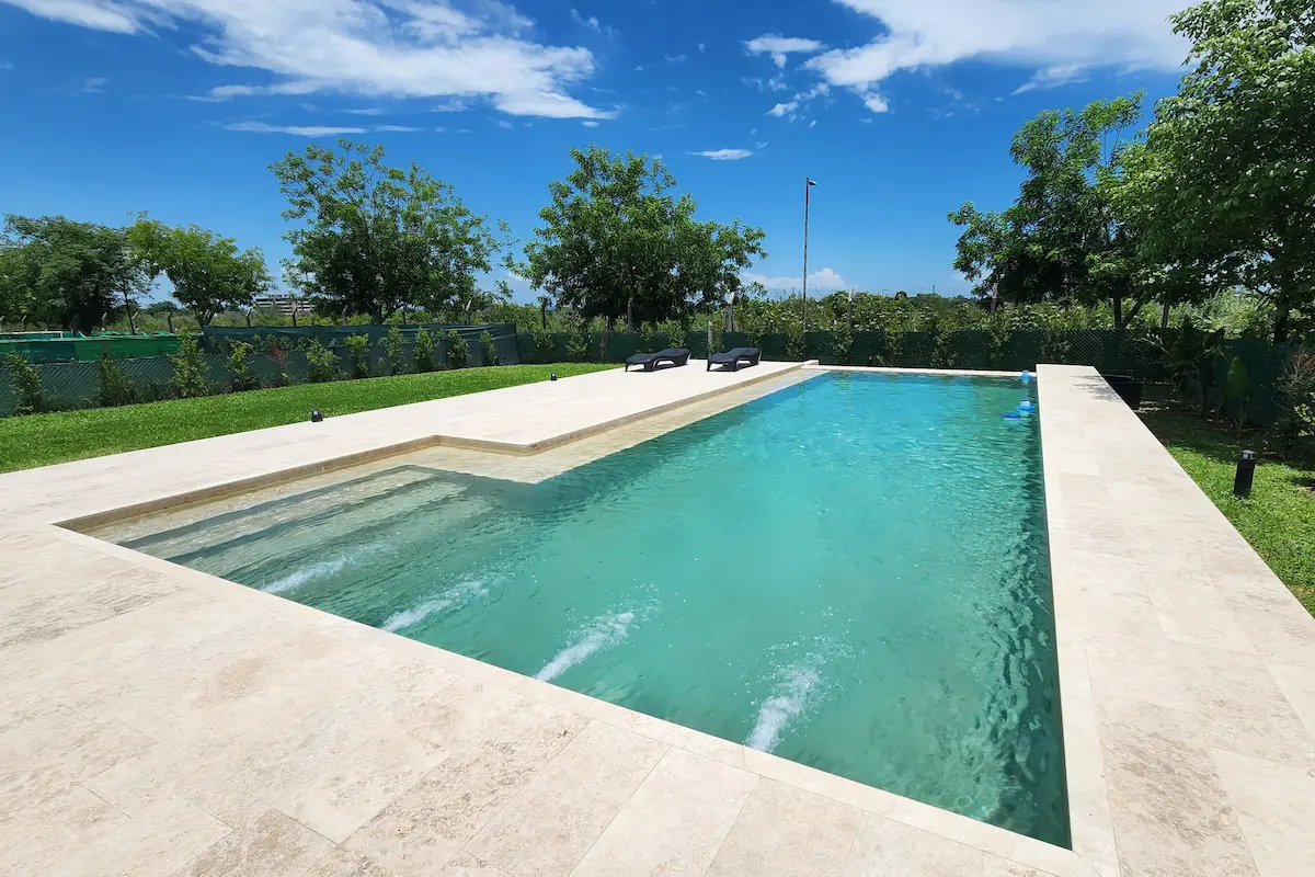 Pileta borde infinito con revestimiento travertino y solarium — Country Praderas, Yerba Buena, Tucumán